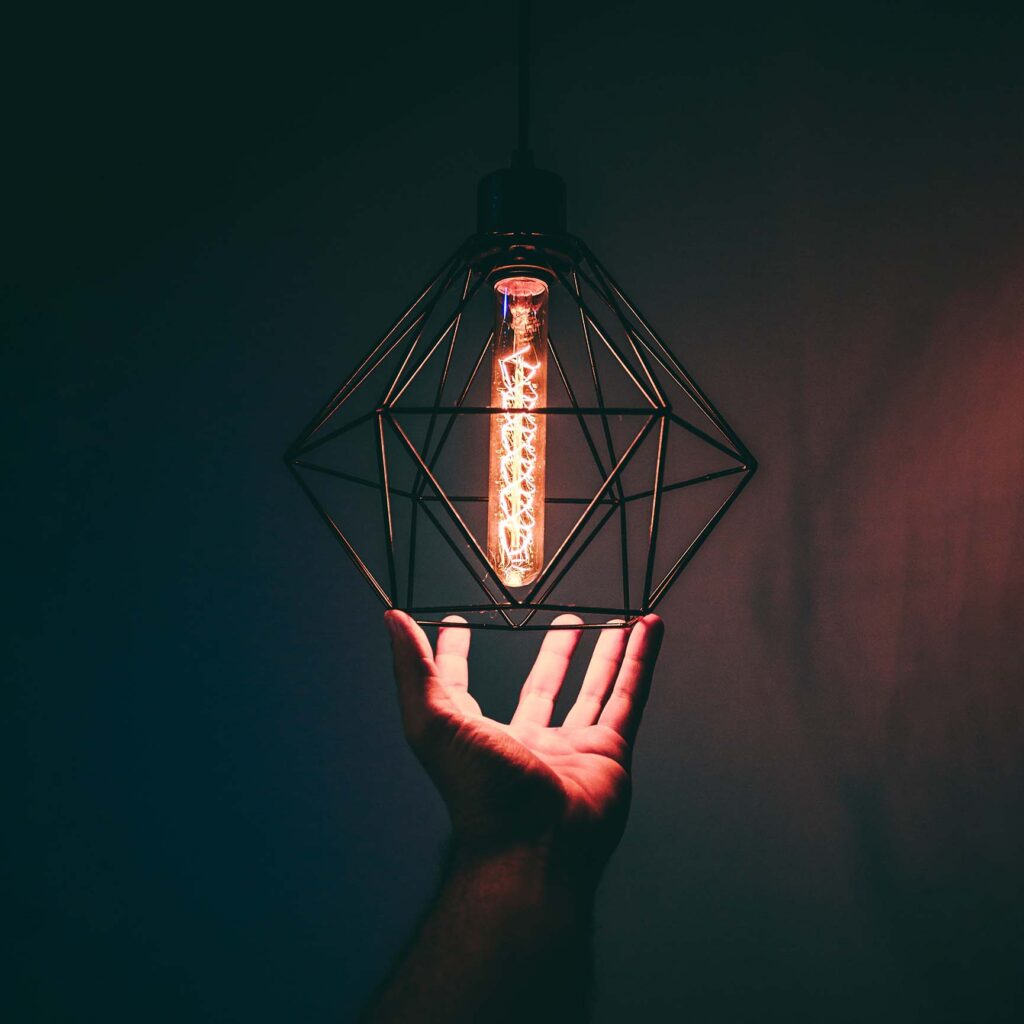 hand holding a geometric lamp shade with a long lightbulb in the center